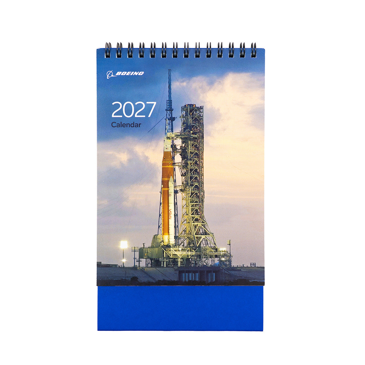 The BOEING 2027 Desktop Calendar features a spiral binding, making it ideal for use on your desk. Its cover displays a rocket on a launchpad at dusk, illuminated against a backdrop of dramatic clouds.