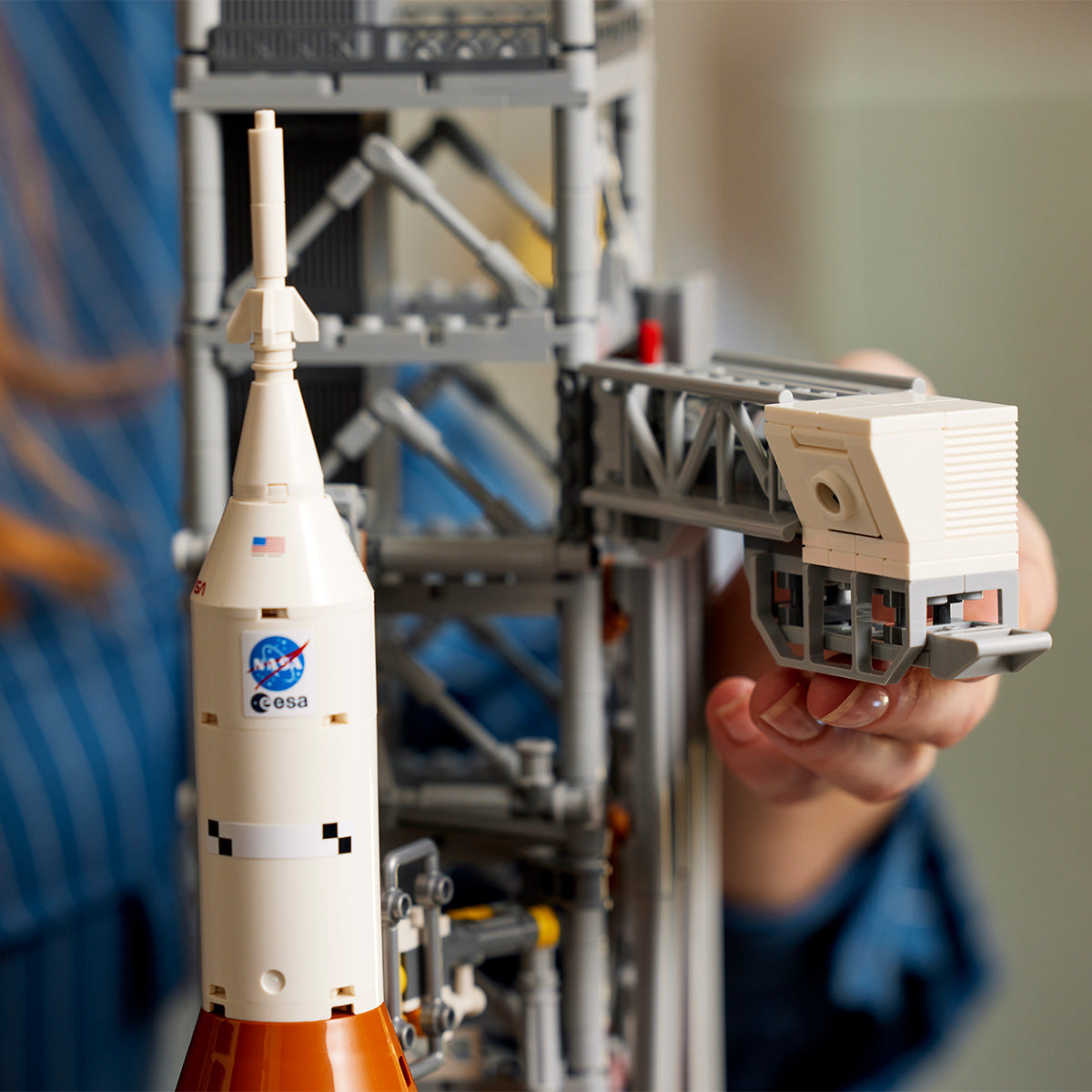 A person in a blue striped shirt holds the LEGO® NASA Artemis SLS Set by LEGO, showing the detailed multistage rocket and launchpad with visible NASA and ESA logos.