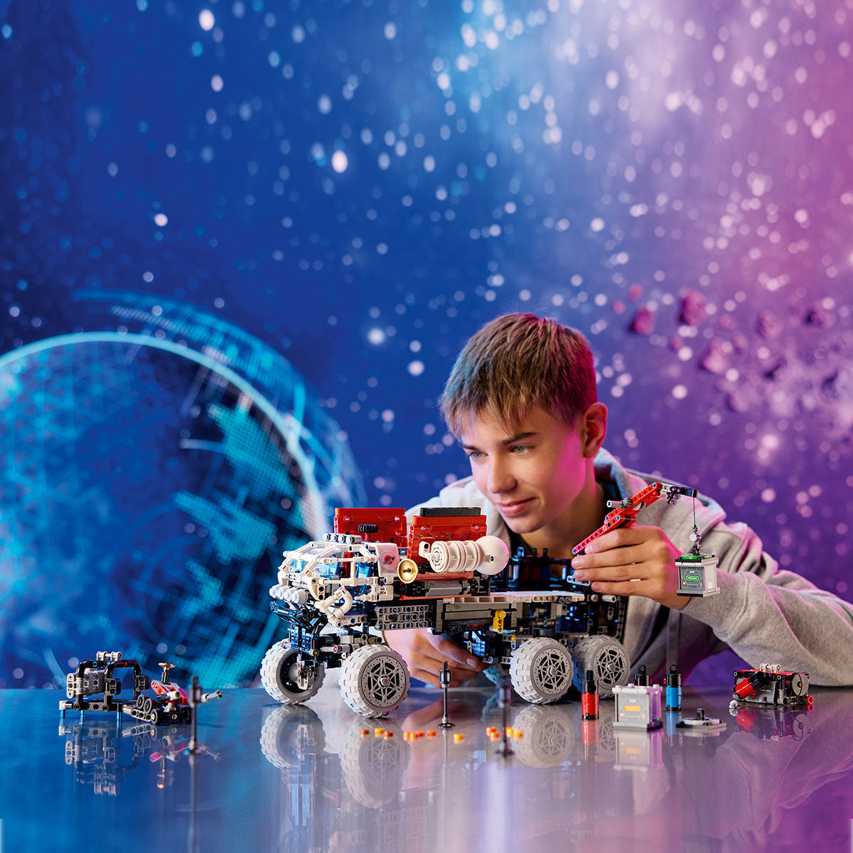 A boy builds the detailed LEGO® Mars Crew Exploration Rover by LEGO on a shiny table, surrounded by a vivid space-themed backdrop—an ideal choice for any fan’s space toy collection.