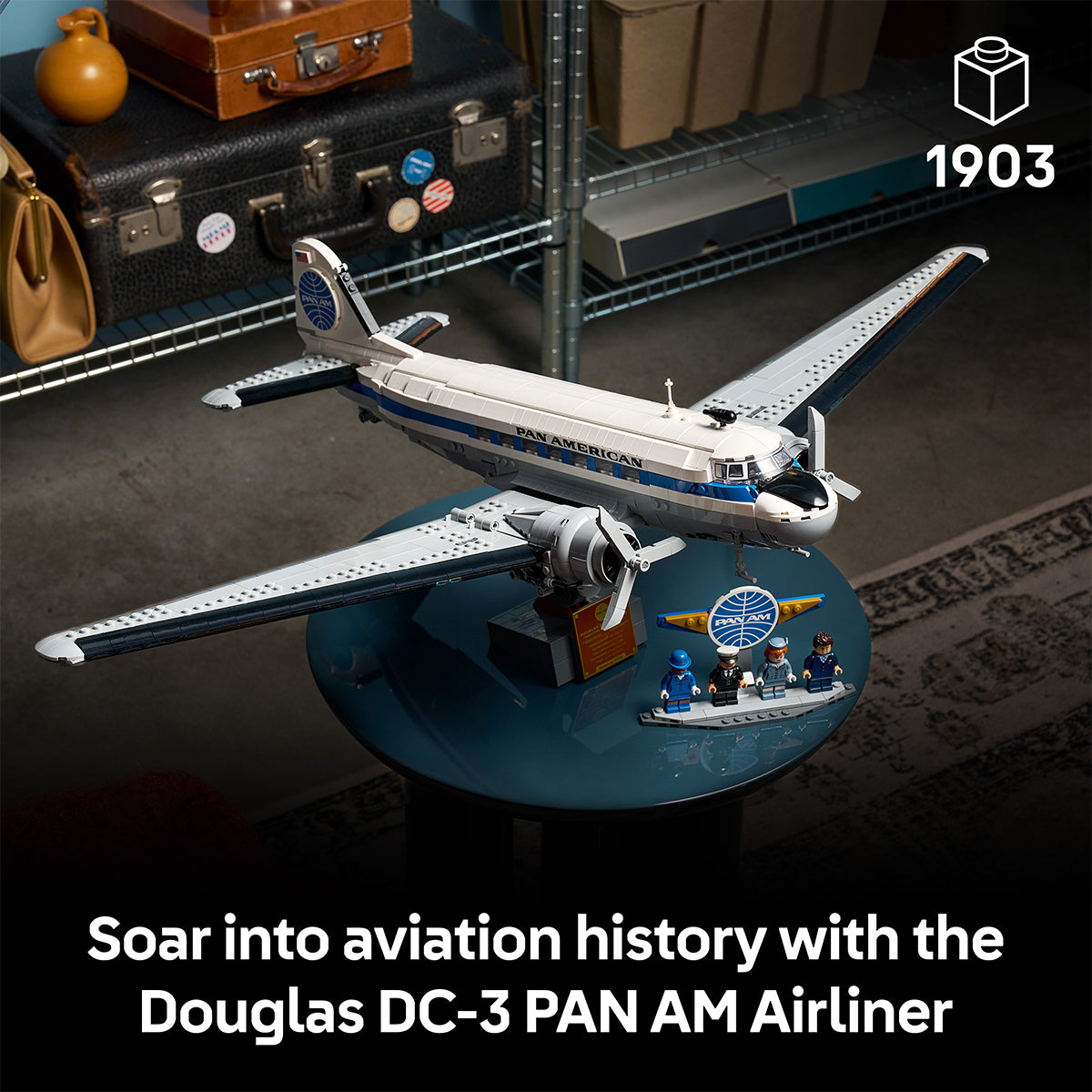A LEGO® Boeing Douglas DC-3 PAN AM Airliner by BOEING is showcased on a round table with mini figures and aviation accessories, set among industrial shelves and luggage. Text: Soar into aviation history with the PAN AM Airliner.