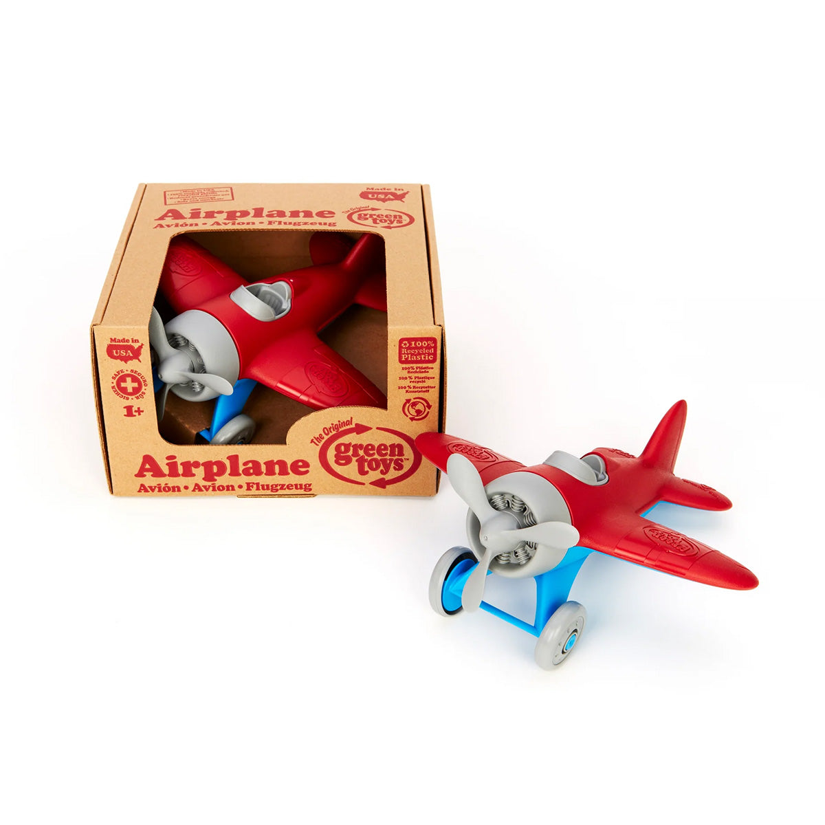 The Green Toys Airplane - Red, made from recycled materials with vibrant red wings, a silver propeller, and blue wheels, is shown beside its cardboard box. The packaging features the GREEN TOYS logo and emphasizes the airplanes non-toxic nature.