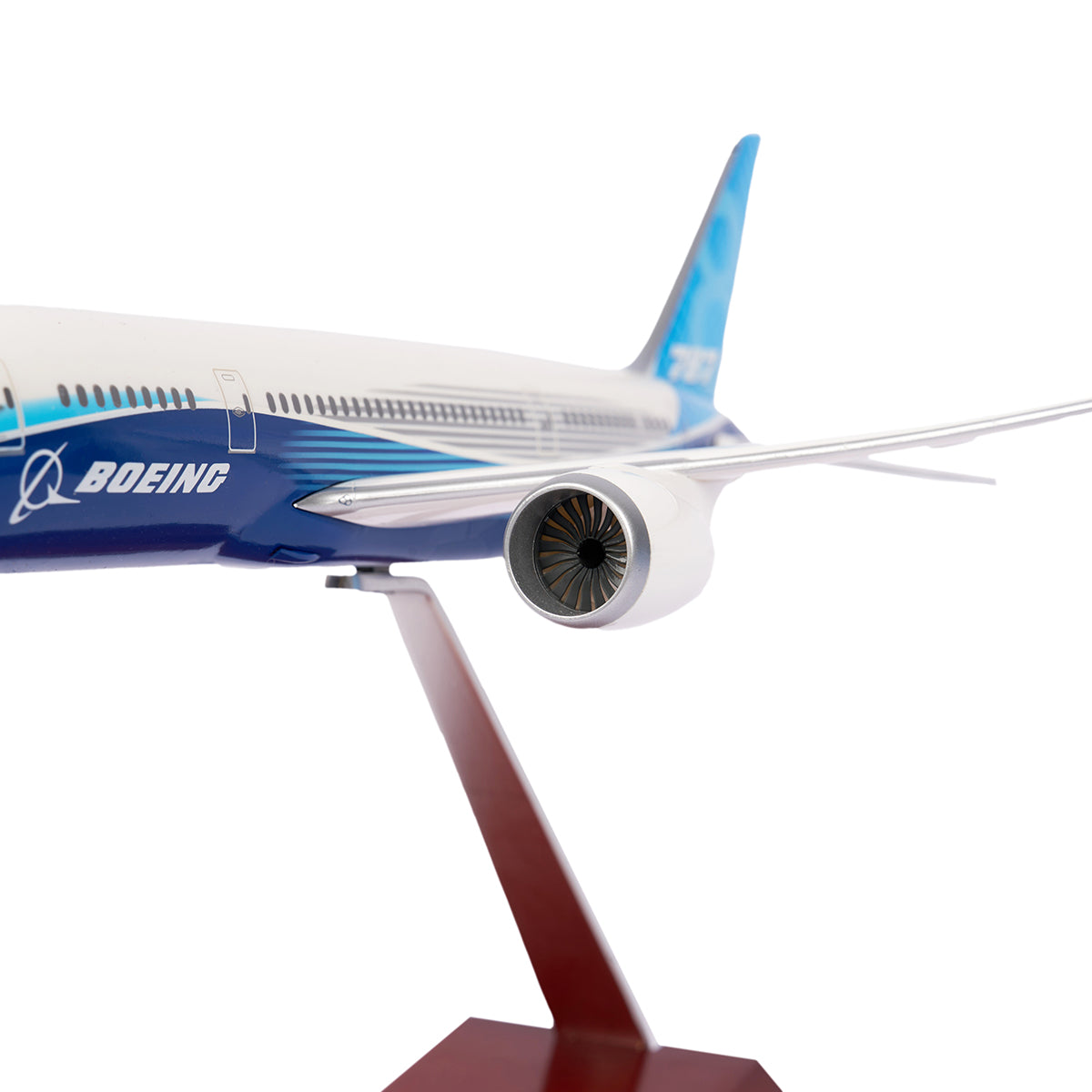 A close-up of The Boeing Stores Boeing Unified 787-8 Dreamliner 1:200 Model on a stand highlights its engine and fuselage with the Boeing logo. This model showcases a sleek, modern aviation design with an elegant white and blue paint scheme.