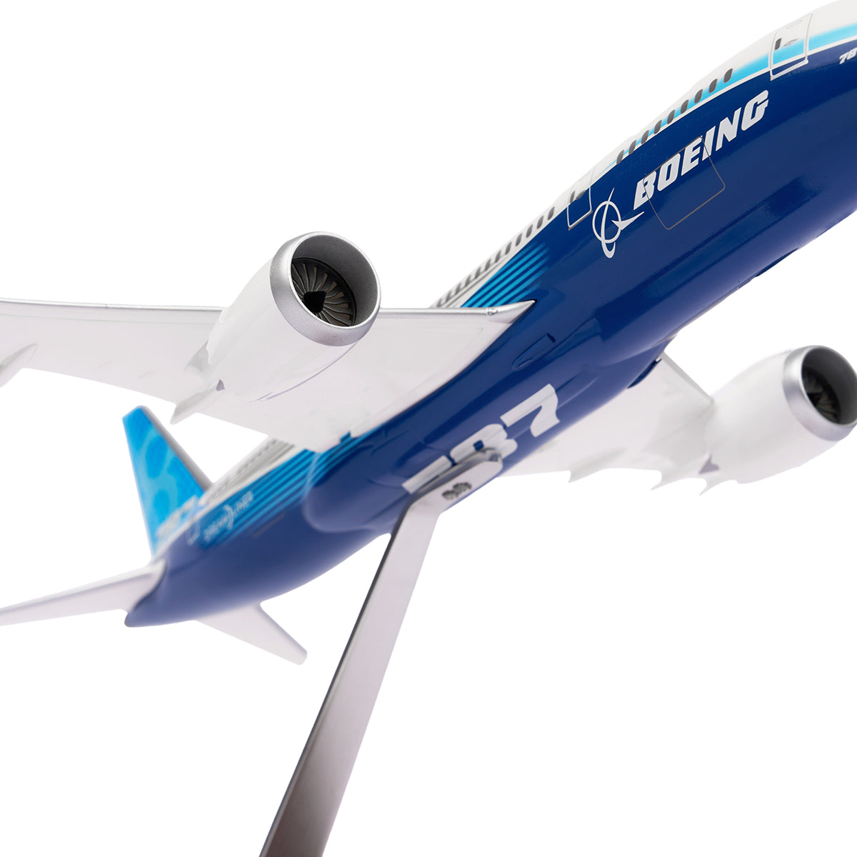 A Boeing Unified 787-8 Dreamliner 1:200 Model from The Boeing Store is mounted on a stand. Viewed from below, the model highlights engines and fuselage, with the iconic Boeing logo displayed, epitomizing modern aviation.