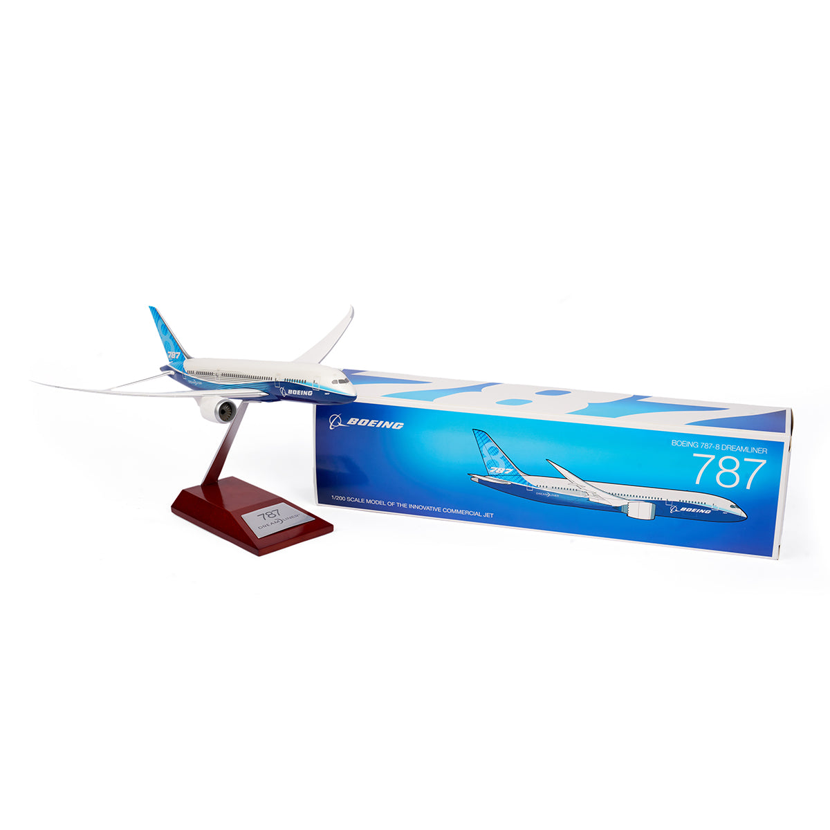 The Boeing Unified 787-8 Dreamliner 1:200 Model from The Boeing Store is displayed on a red stand. This sleek, white model with a blue tail sits next to its blue packaging box adorned with the Boeing logo and an illustration celebrating modern aviation.