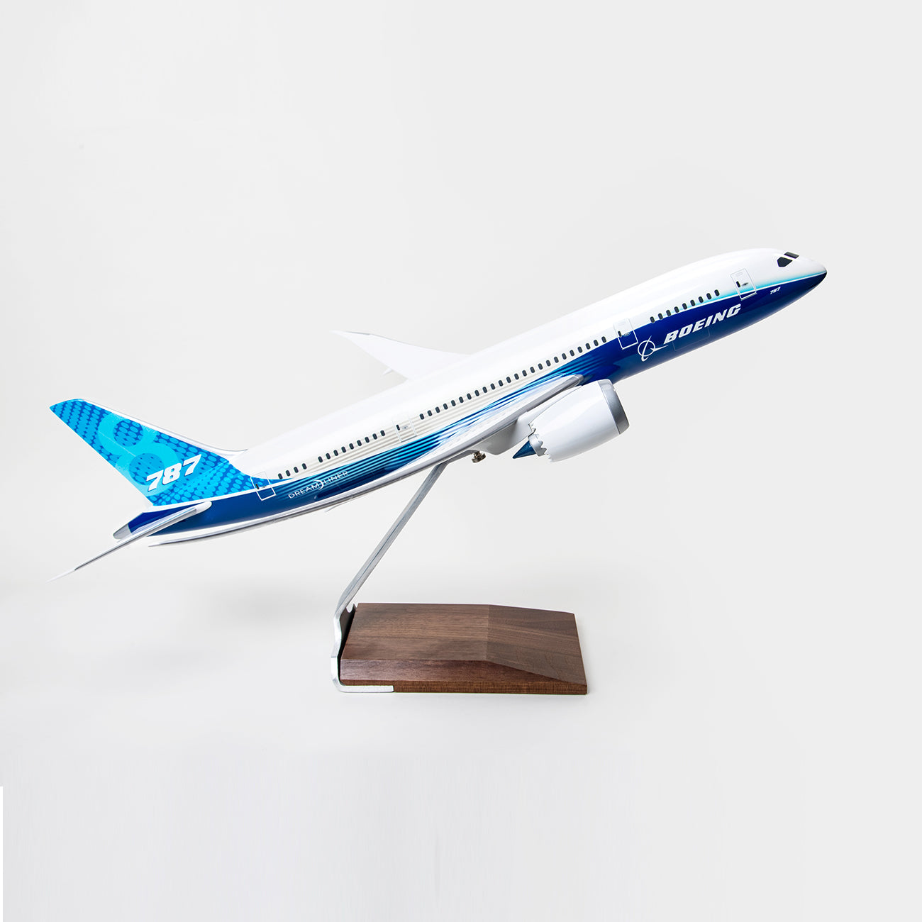 The PACMIN Boeing 787-8 Dreamliner Resin 1:100 Model showcases a blue and white livery, comes with a metal stand and wooden base, and is displayed against a plain white background.