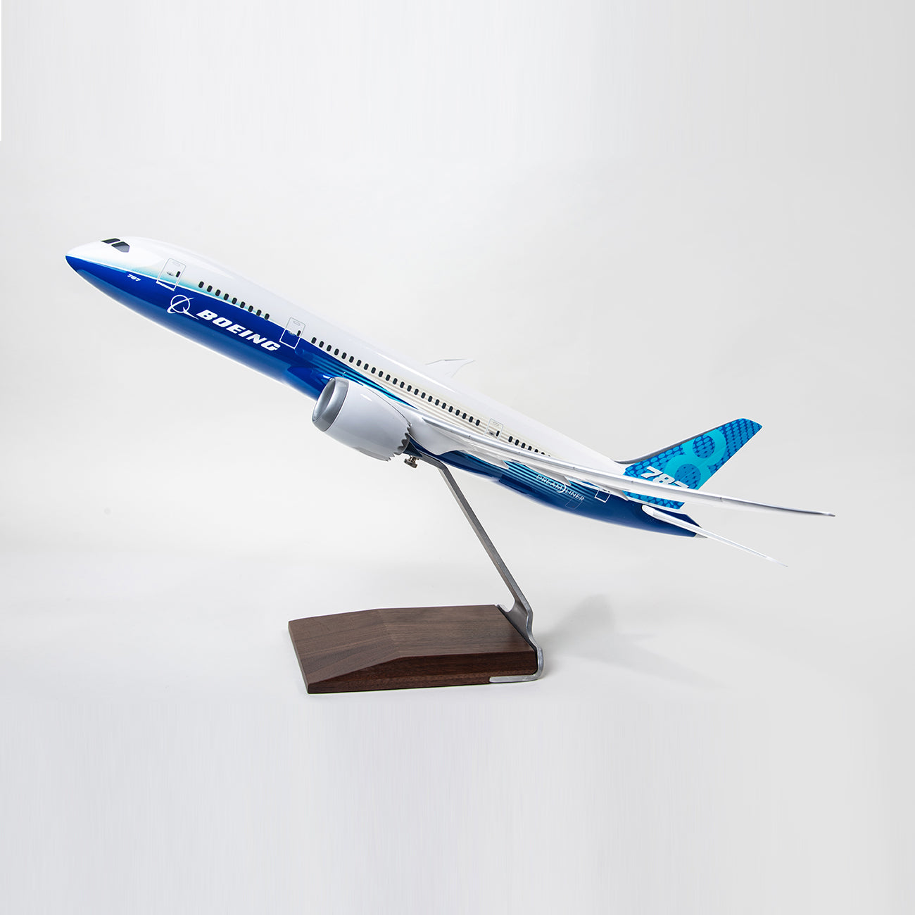 The PACMIN Boeing 787-8 Dreamliner Resin 1:100 Model features blue and white colors, is Boeing-approved, and comes mounted on a stand with a wooden base, set against a plain light background.