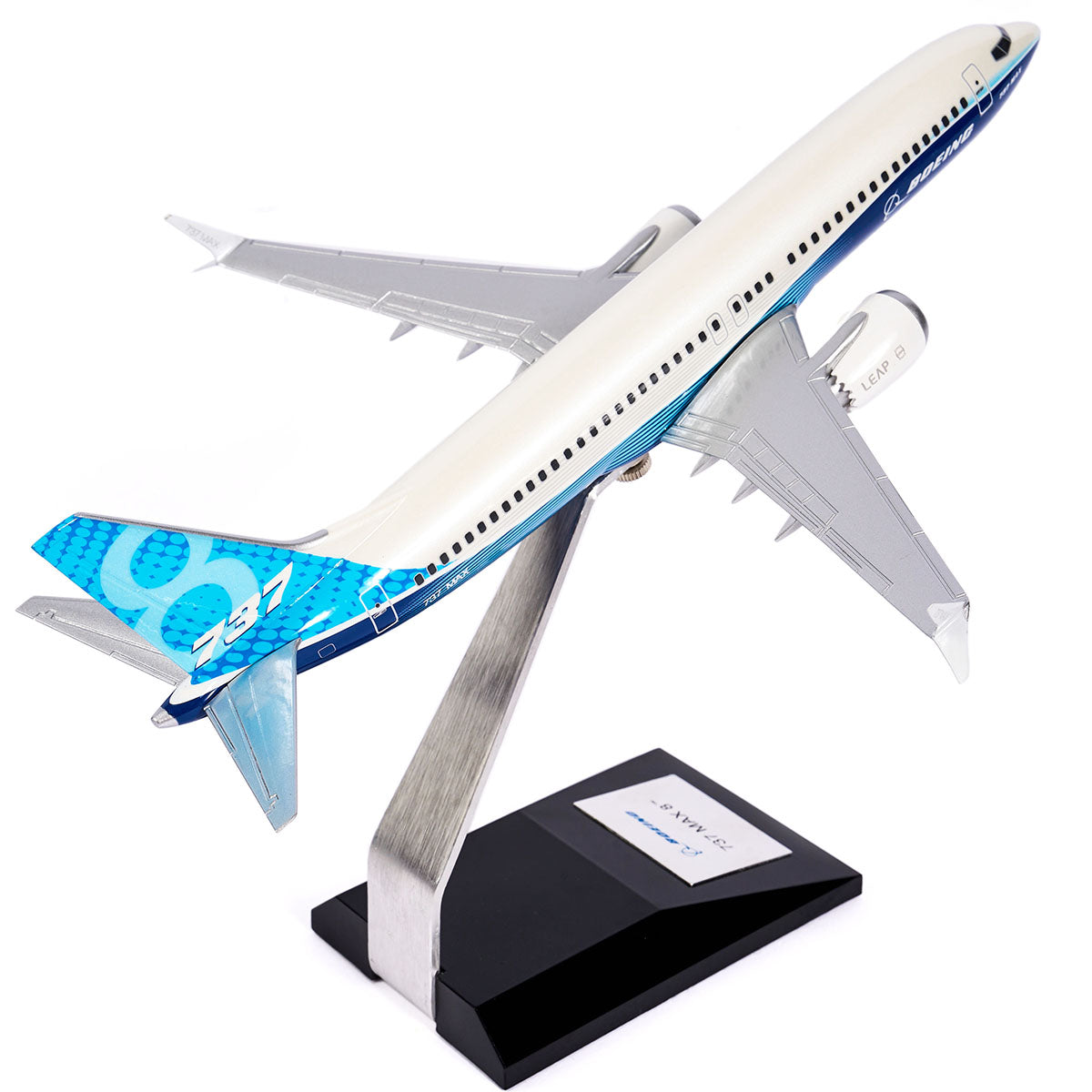 The Boeing Unified 737 MAX 8 model by Pacific Miniatures, crafted from precision injection-molded plastic, features a blue and white design on its angled stand. Its wings and tail display patterns with stylized numbers, while the black base includes a label for identification.