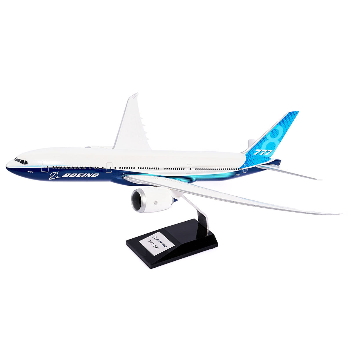 The Boeing Stores Boeing Unified 777-8 1:144 Model features a sleek white and blue design with a distinctive tail fin. Mounted on a black stand with a silver plaque, this model captures the elegance and innovation of modern twin-engine jets.