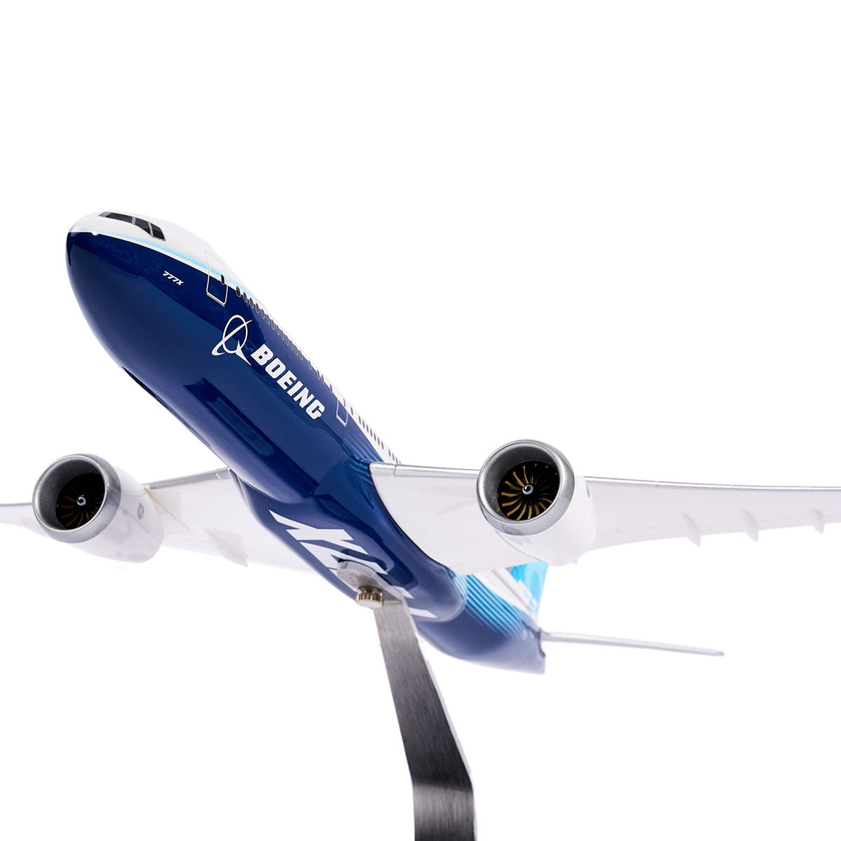 The Boeing Stores Boeing Unified 777-8 1:144 Model features a blue and white twin-engine design, displayed on a stand against a white backdrop to highlight its engines and underbelly.