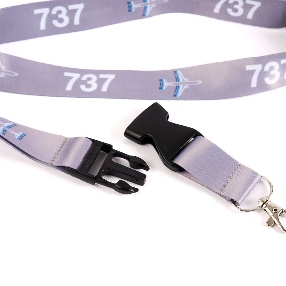 The Boeing Stores Boeing 737 Motion Lanyard is a gray aviation-inspired accessory with white 737 sublimation and blue airplane graphics. It features a detachable black plastic buckle and a metal swivel hook.