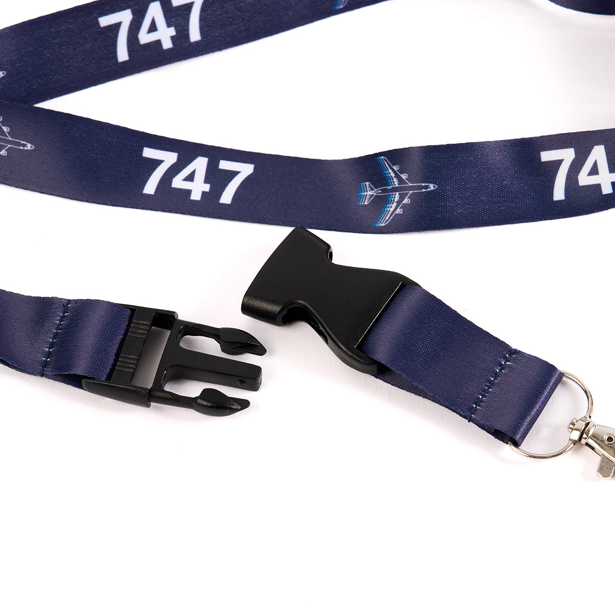 The Boeing 747 Motion Lanyard from The Boeing Store features a dark blue design with aviation-inspired 747 sublimation prints and airplane graphics. It includes a detachable black plastic buckle and a metal keyring loop, ideal for aviation enthusiasts.