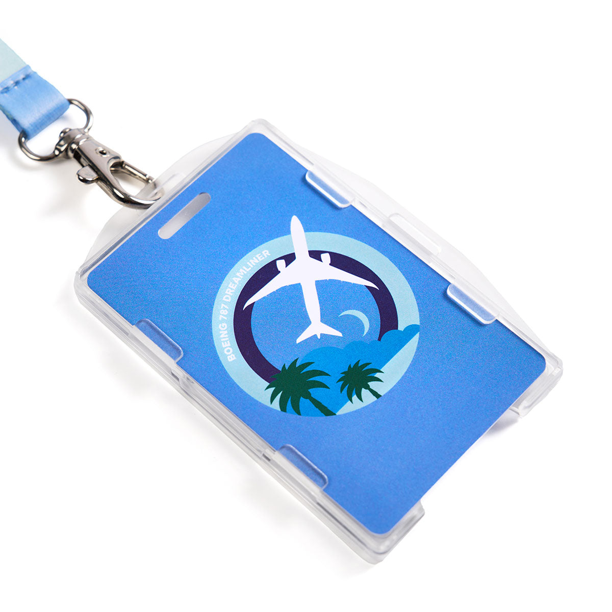 The Boeing 787 Dreamliner Skyward Lanyard by Boeing is blue with a sublimation print of a white airplane soaring over palm trees and a crescent moon, while Boeing 787 Dreamliner is elegantly displayed in the clear plastic badge holder.