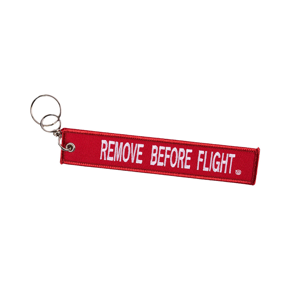 The Boeing T-7A Remove Before Flight Keychain, a red fabric tag with bold white REMOVE BEFORE FLIGHT lettering, includes a sturdy metal keyring. Ideal for aviation enthusiasts or frequent flyers.