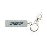 The BOEING 767 Series Keychain is a light gray, rectangular rubber accessory featuring "767" in bold, dark blue, embossed lettering. This aviation-themed keychain comes attached to a silver metal split ring and a lobster claw clasp, all showcased against a plain white background.