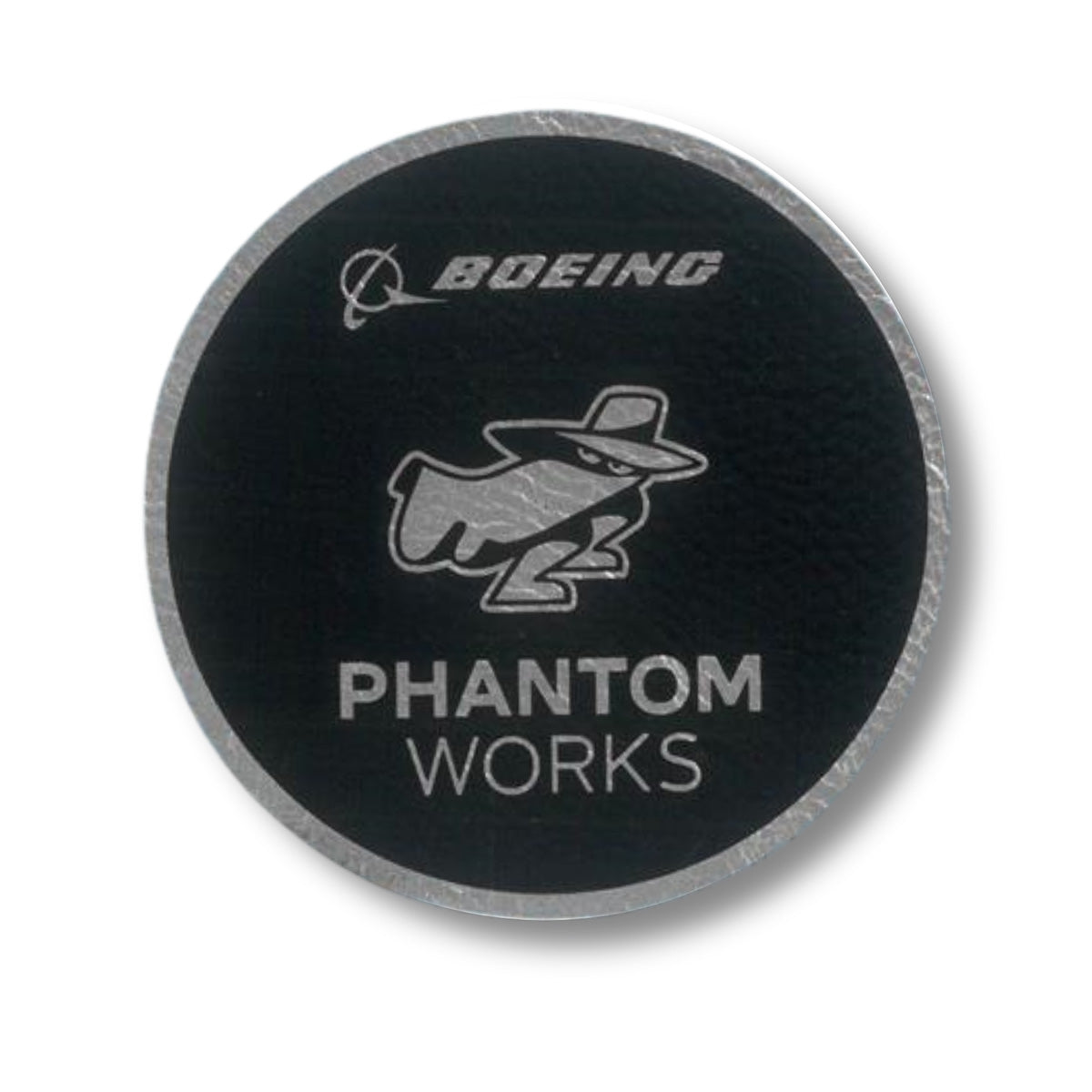 The Boeing Phantom Works 2025 Patch by BOEING features a circular black design with a mysterious figure in a hat and cape, and "PHANTOM WORKS" in silver below—an eye-catching collectible for Boeing fans.