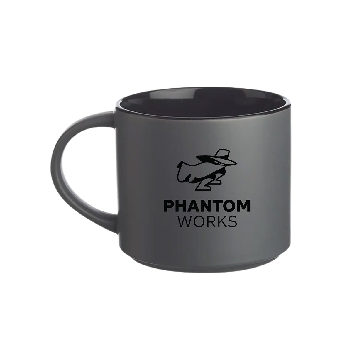 The Boeing Phantom Works Ceramic Matte Mug by BOEING features a matte gray ceramic exterior with a black interior and showcases a stylized figure in a hat and trench coat above the PHANTOM WORKS text, making it an ideal aerospace gift for Boeing fans.