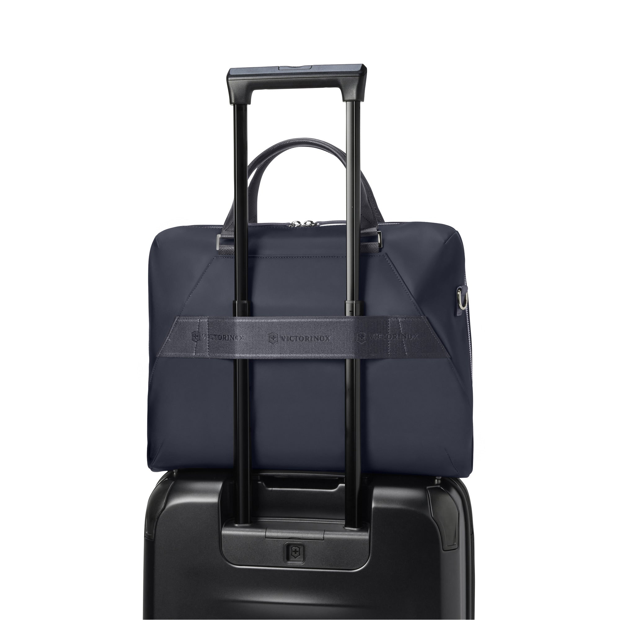 A navy blue Victorinox Victoria Signature Briefcase with cushioned leather handles is securely placed on a black rolling suitcase. Part of a 2-in-1 setup, it attaches to the suitcases extended handle via a horizontal strap for hassle-free travel.