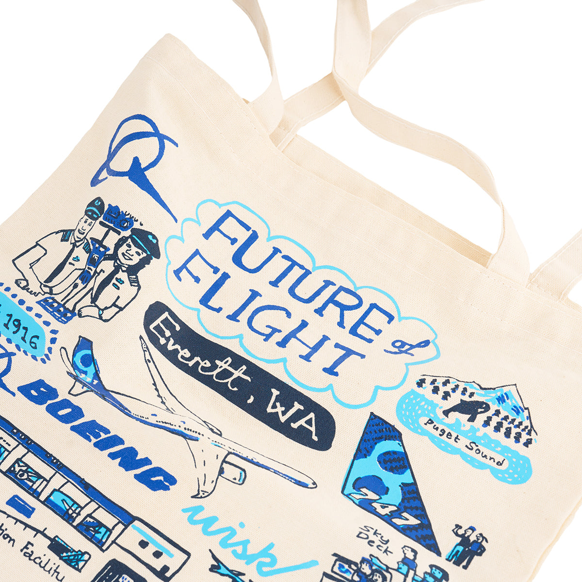 The BOEING Future of Flight Destination Canvas Tote Bag in cream features blue aviation-inspired graphics and text, including “Future of Flight,” “Everett, WA,” a Boeing plane, pilots, mountains, and more.