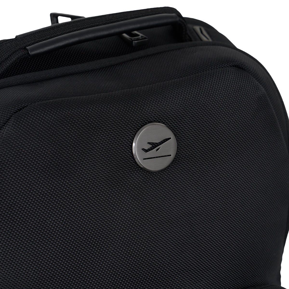 A close-up of the MyGoFlight Elevate Bag by BOEING, made from durable black ballistic nylon and featuring a round metal emblem with an airplane symbol on the front.