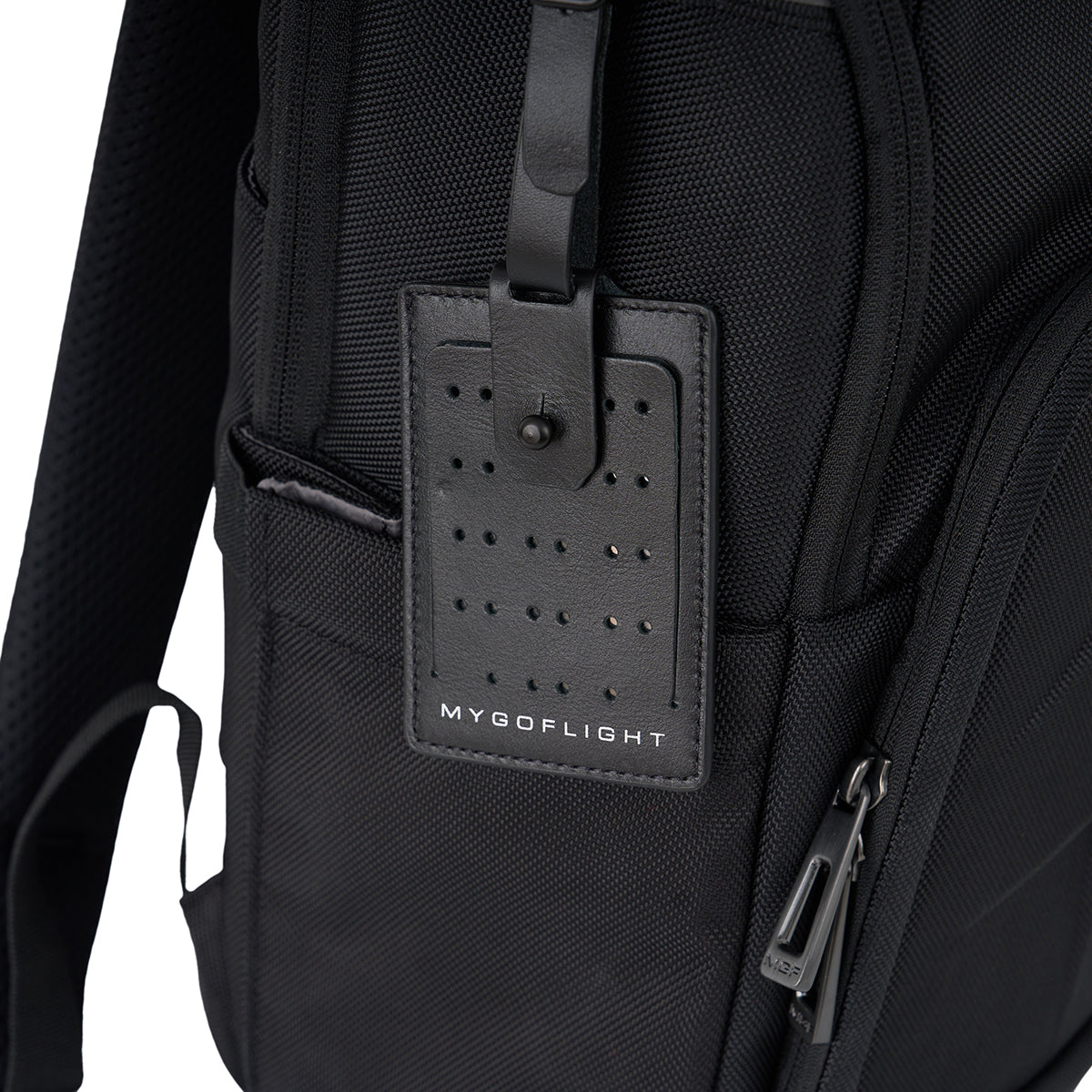 Close-up of a rugged BOEING MyGoFlight Elevate Bag with a leather luggage tag featuring perforated holes and branding. A zipper and shoulder strap are also visible on this aviation pilot backpack.