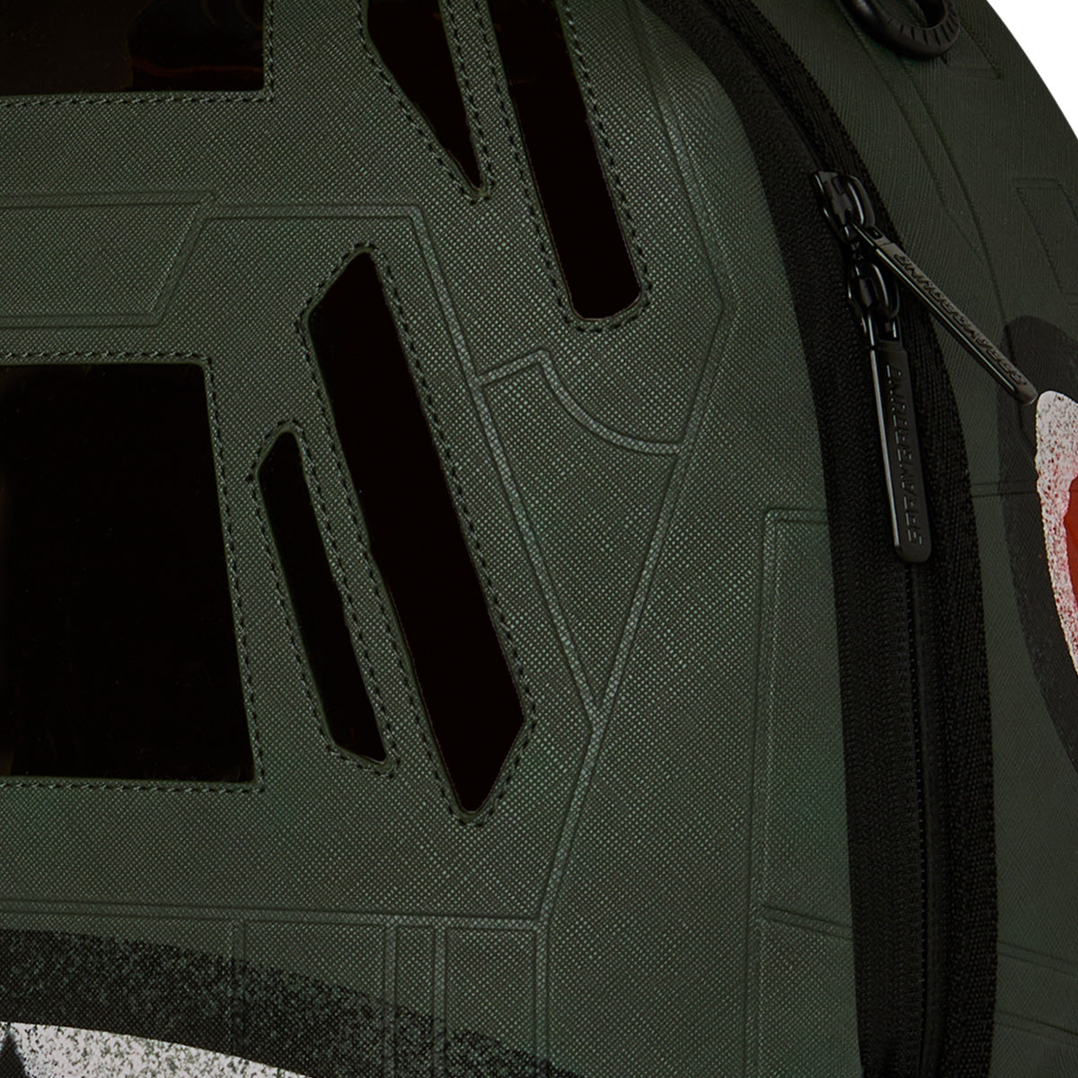 Close-up of the Sprayground Boeing AH-64 Apache Sharkmouth DLXSV Backpack by BOEING, showcasing its green color adorned with black geometric shapes and patterns. The design features a zipper on the right side and textured fabric material, drawing inspiration from tactical styling for a rugged yet modern aesthetic.