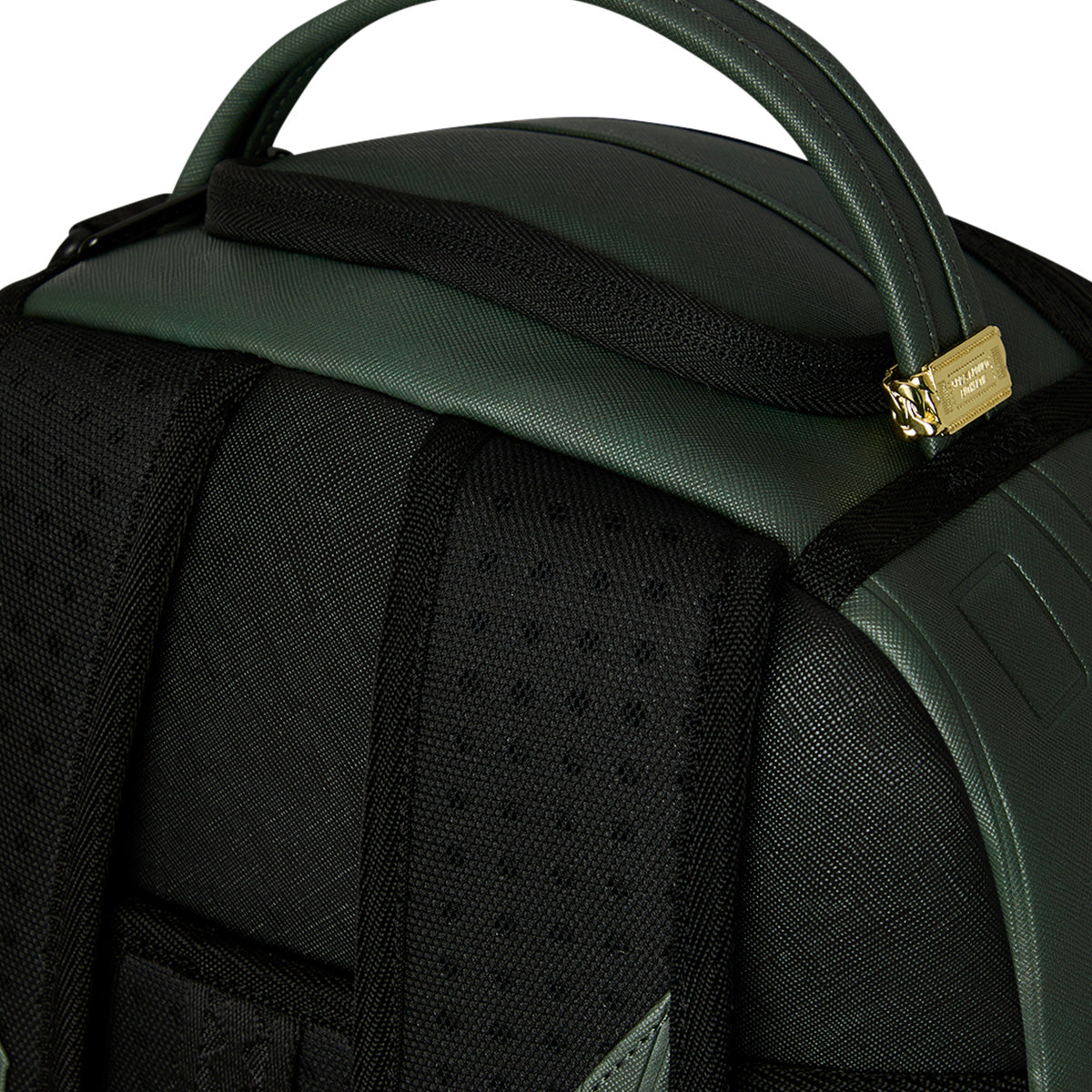 Close-up of the Sprayground Boeing AH-64 Apache Sharkmouth DLXSV Backpack’s top handle, gold zipper, and black padded shoulder straps featuring perforated detailing. The materials from BOEING appear durable and textured, highlighting subtle tactical styling.