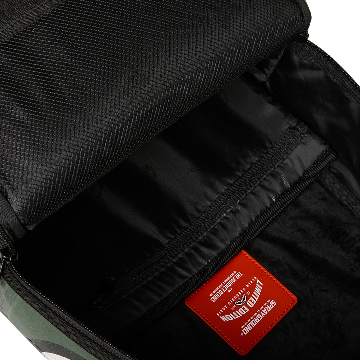 Open BOEING Sprayground Boeing AH-64 Apache Sharkmouth DLXSV Backpack displaying a zippered inner pocket, black lining, and a red label with white text near the bottom inside, highlighting its tactical styling.