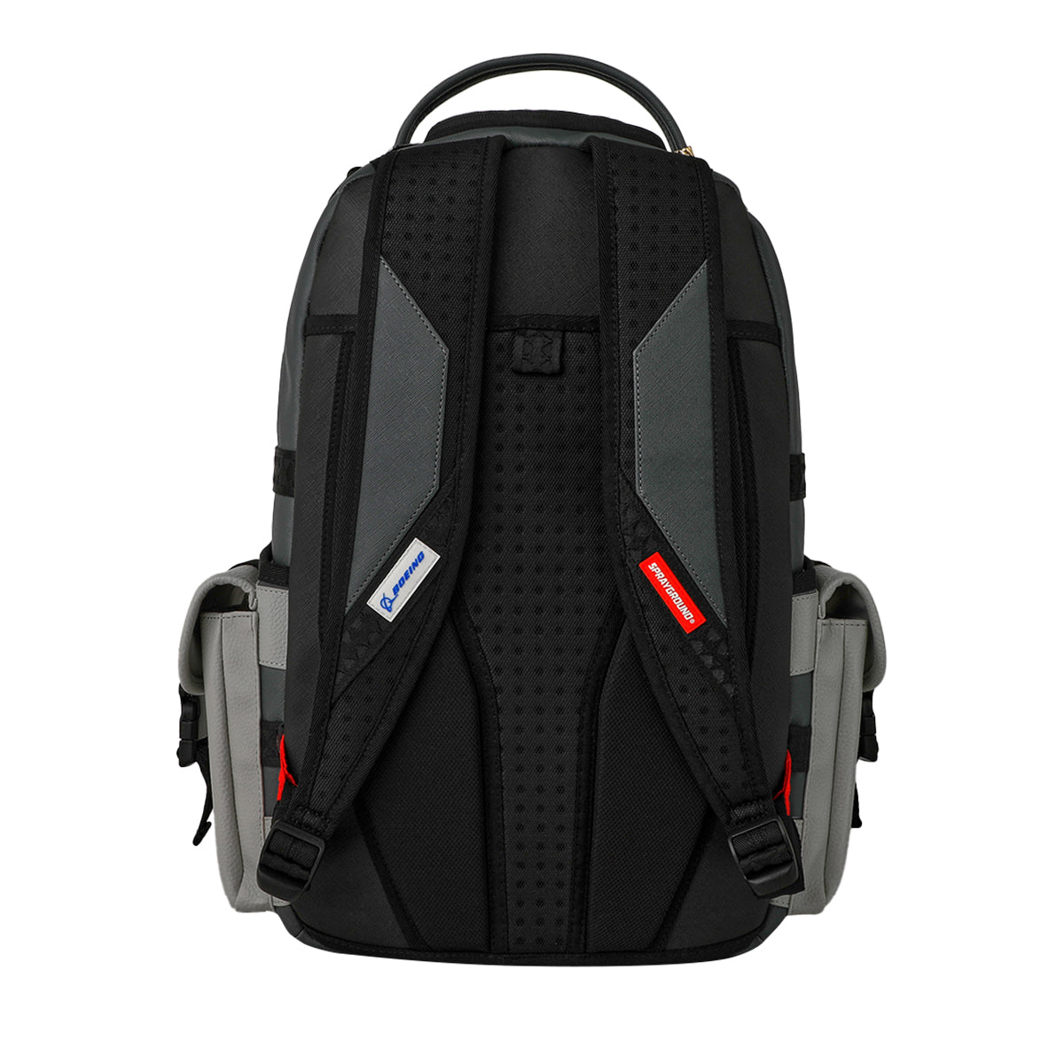 A back view of the Sprayground Boeing C-17 Globemaster DLXSV Backpack by BOEING highlights its black and gray color scheme, padded straps with small colored tags, side pockets, and a top handle. The backpack showcases a sporty, modern design inspired by military aesthetics.