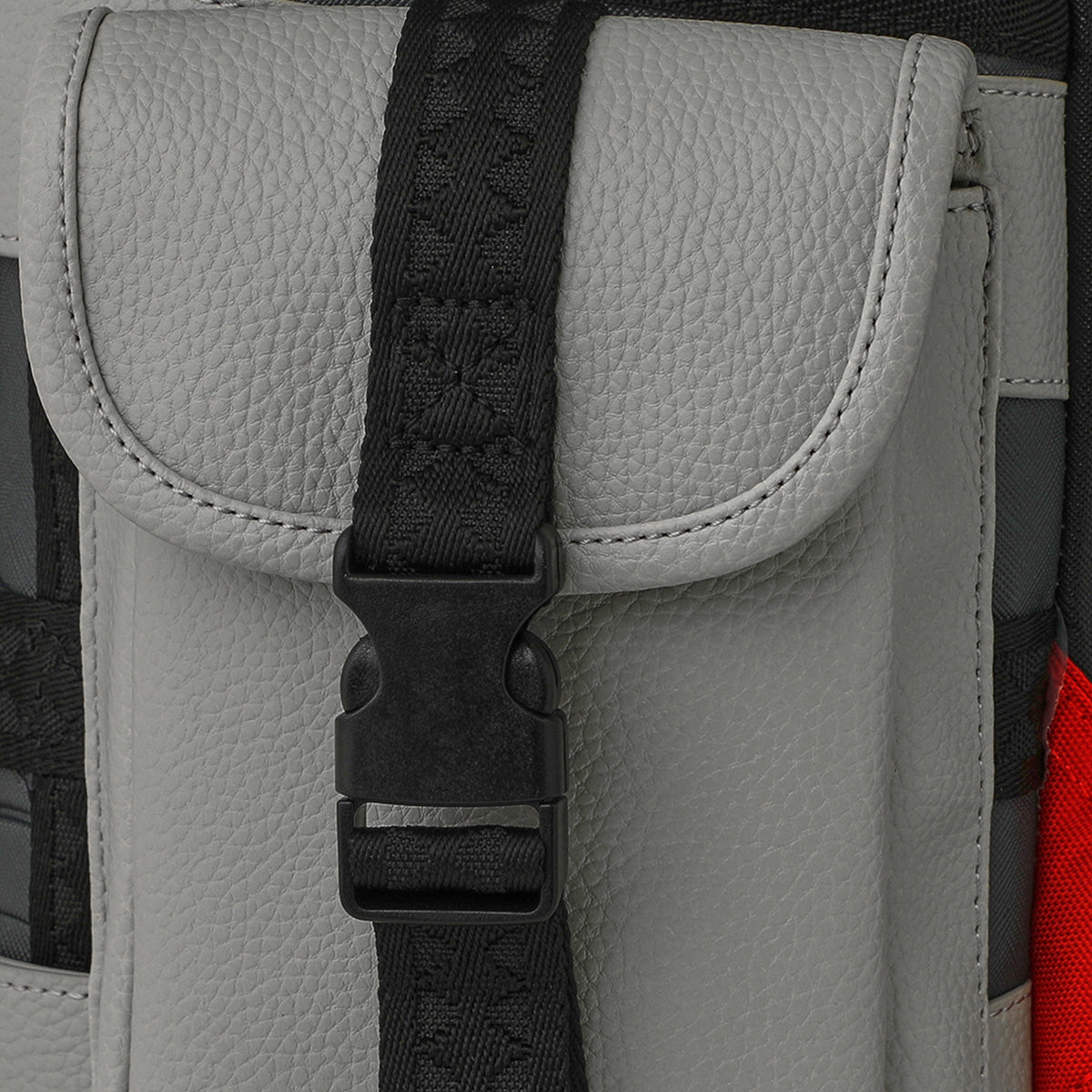 Close-up of a gray textured BOEING Sprayground Boeing C-17 Globemaster DLXSV Backpack pocket featuring a black strap and plastic buckle at the center. A touch of red fabric is visible along the right edge, accentuating its military-inspired design.