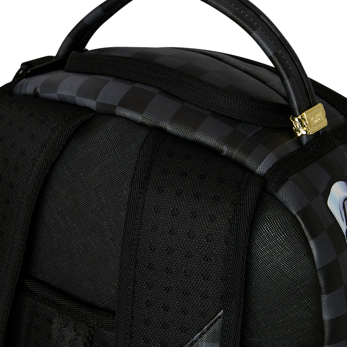 Close-up of a black Sprayground Boeing P-51 Mustang Sharkmouth DLXSV Backpack featuring padded straps, a checkered top panel, and a gold zipper. The handle and part of the back panel are visible, showcasing the sleek design inspired by the Boeing logo for this exclusive collaboration with BOEING.