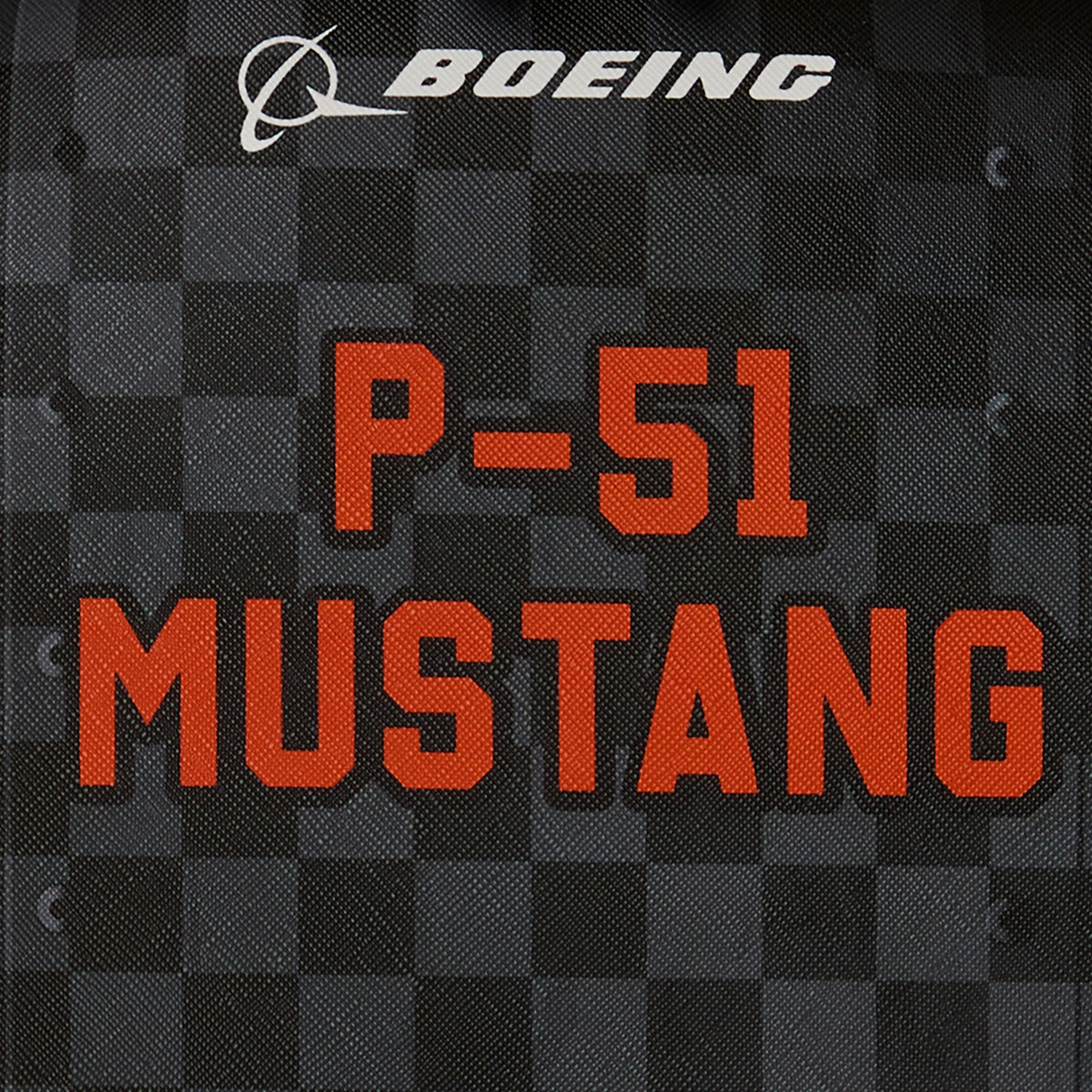 BOEING logo above bold red text reading "P-51 Mustang Sharkmouth" on a textured dark checkered background, capturing the spirit of flight in this unique Sprayground Boeing P-51 Mustang Sharkmouth DLXSV Backpack.