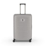 Meet the VICTORINOX Airox Advanced Large - Stone: a sleek suitcase featuring a grey hard shell with horizontal ridges, telescopic handle, and four spinner wheels. Its anti-microbial interior ensures cleanliness, while the brand logo is prominently displayed on the front against a plain white background.