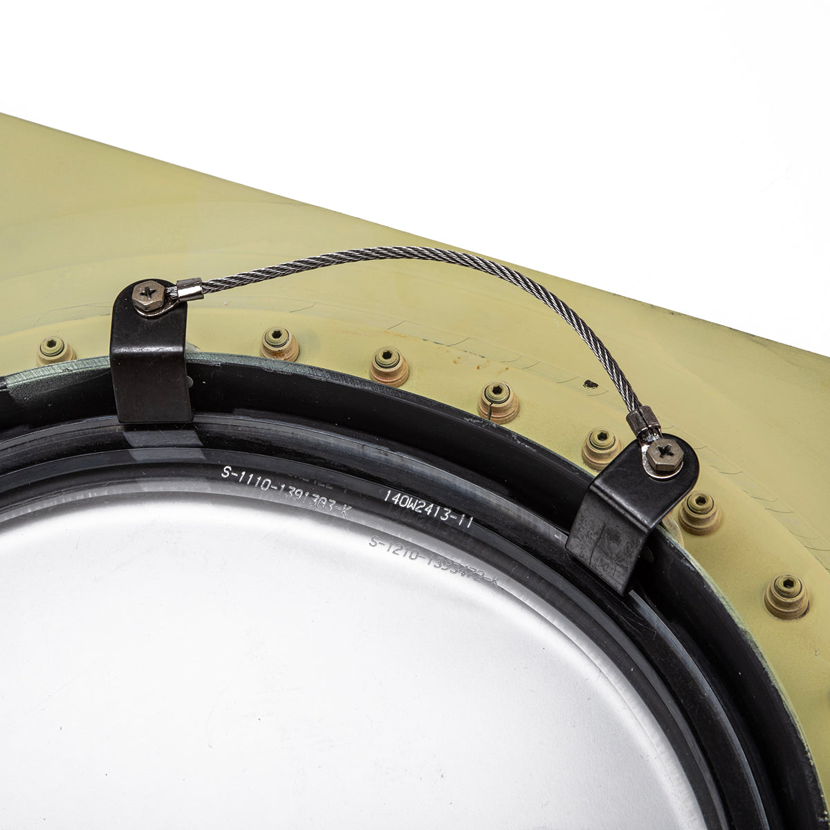 Close-up of a Boeing 777 Natural Finish Window by Boeing, bolted onto a green surface with a thick cable secured by two black screw-fixed brackets crossing over the top of the panel.