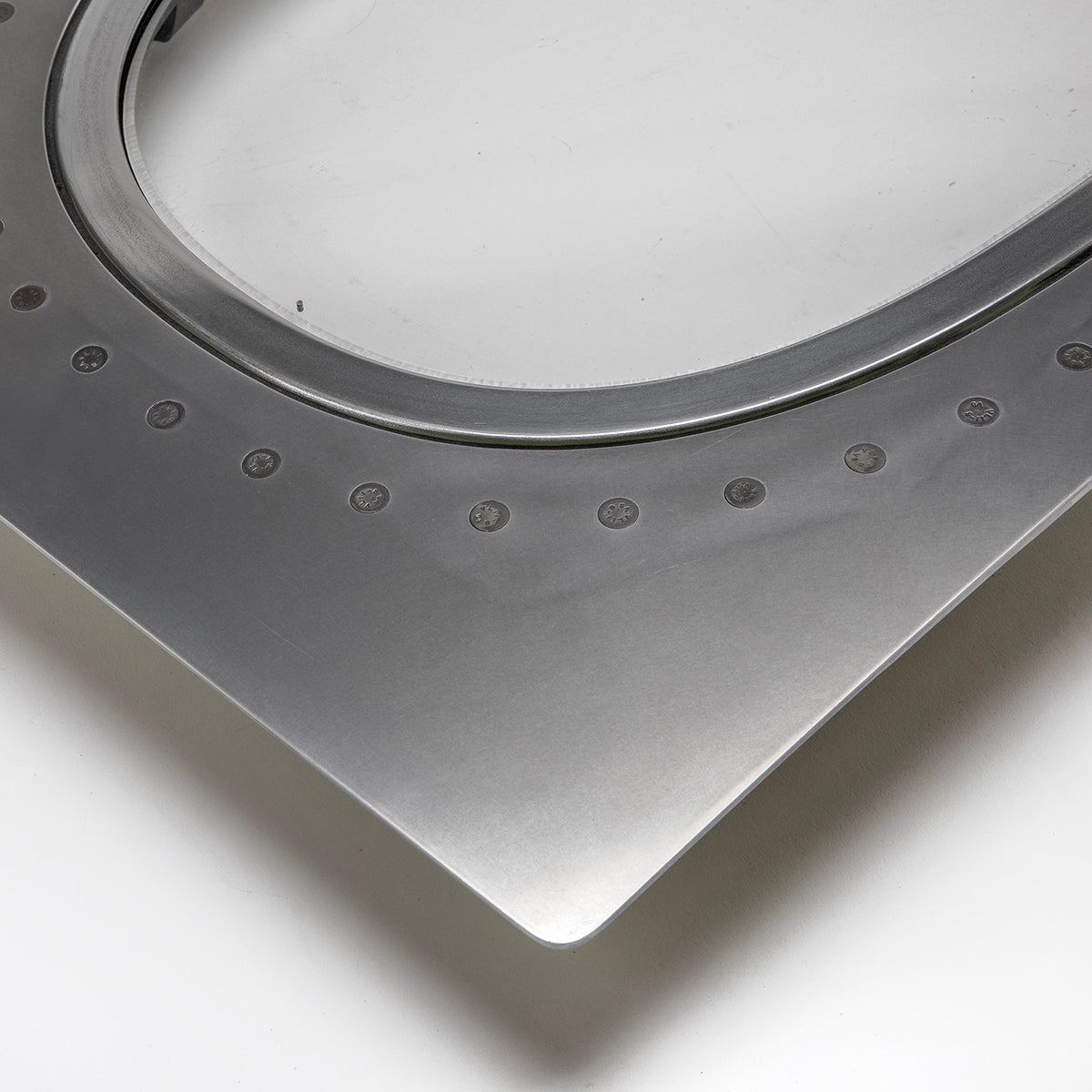 Close-up of a Boeing 777 Natural Finish Window by Boeing, showing a metallic curved edge with evenly spaced circular indents, photographed on a white background.