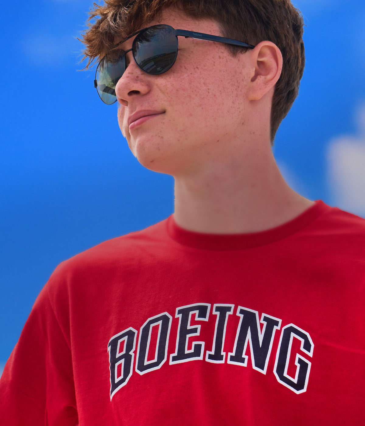 Mobile banner featuring a young man wearing a red t-shirt with "Boeing" printed on it, posed against a blue sky background.
