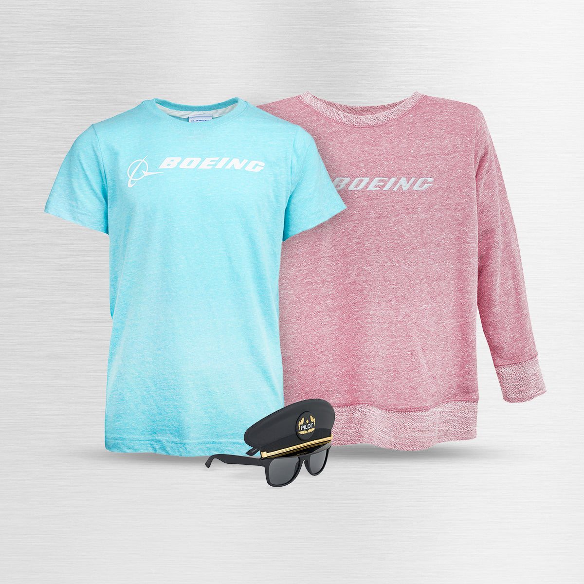Two pieces of Boeing kids' apparel: a light blue t-shirt and a red sweatshirt, accompanied by a pair of pilot sunglasses, displayed on a sleek silver background.