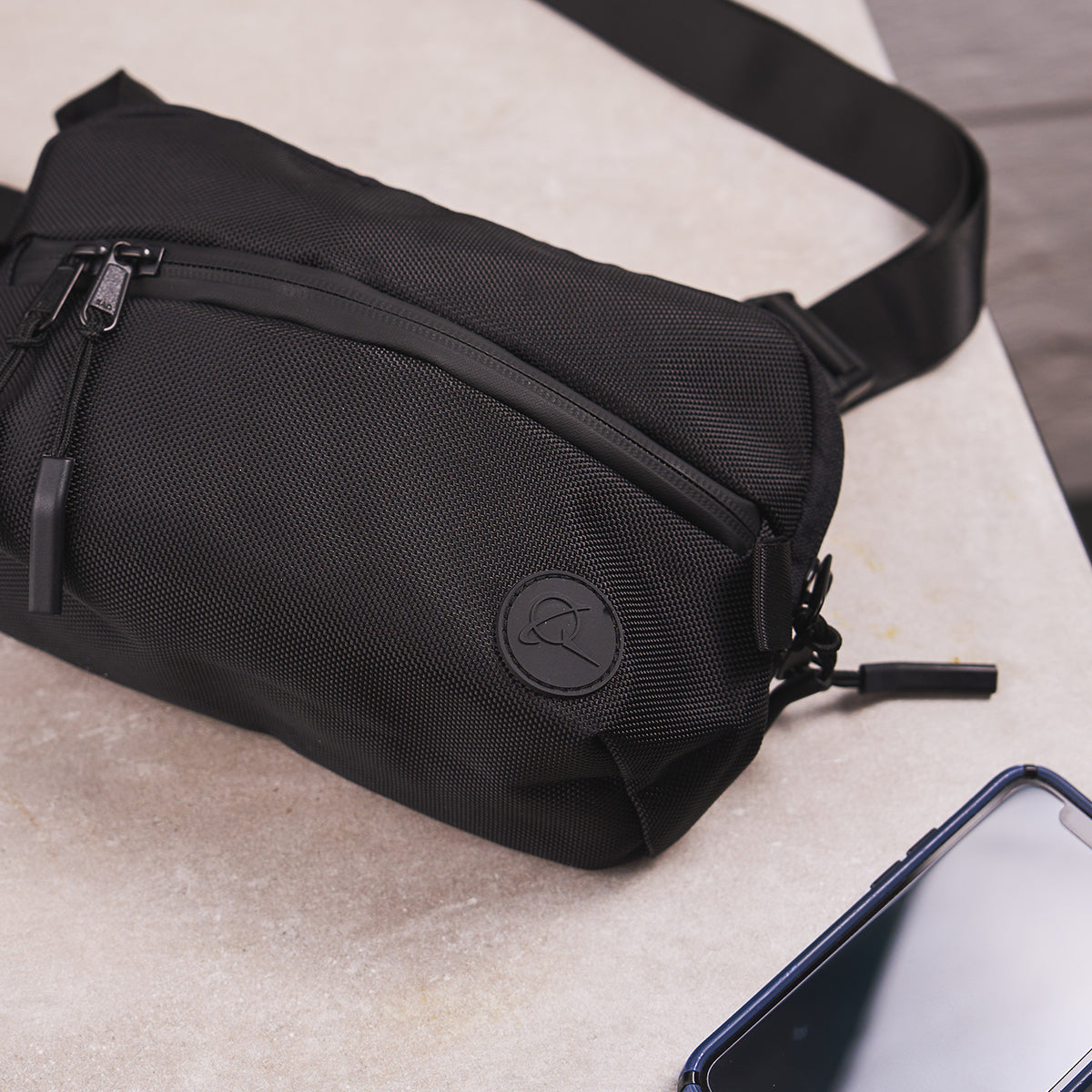 A compact black sling bag  featuring the Boeing Symbol logo with a zippered pocket, ideal for carrying essentials.