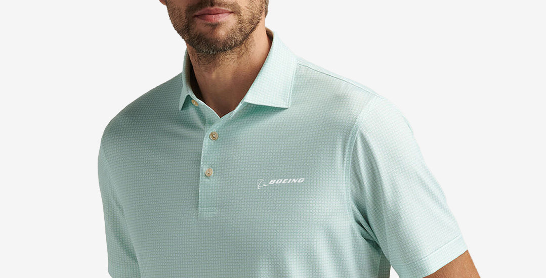 Collection List tile with man wearing a green Peter Millar performance polo on a grey background. Maps to men's apparel.