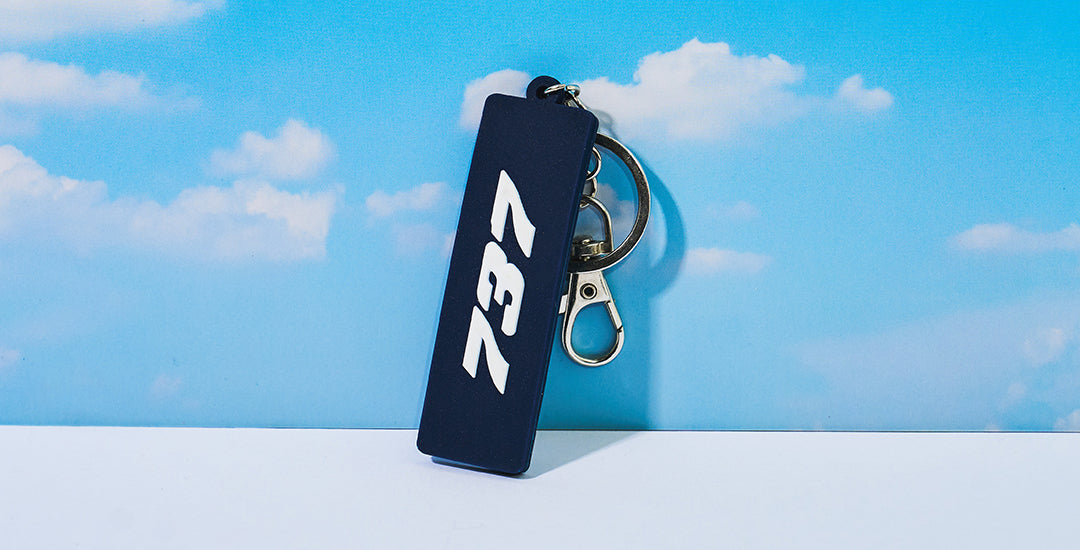 Boeing 737 Series keychain with logo on front against a bright blue sky with clouds.