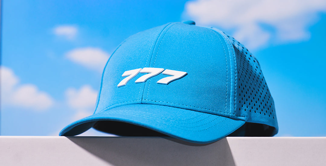 Boeing 777X Series Hat with logo on front against a bright blue sky with clouds.