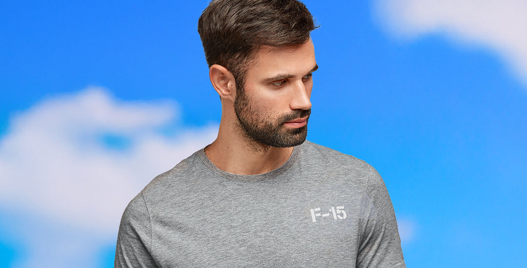 A person wearing a grey Boeing Series T-shirt with the F-15 logo on the left chest, standing against a blue sky with clouds.