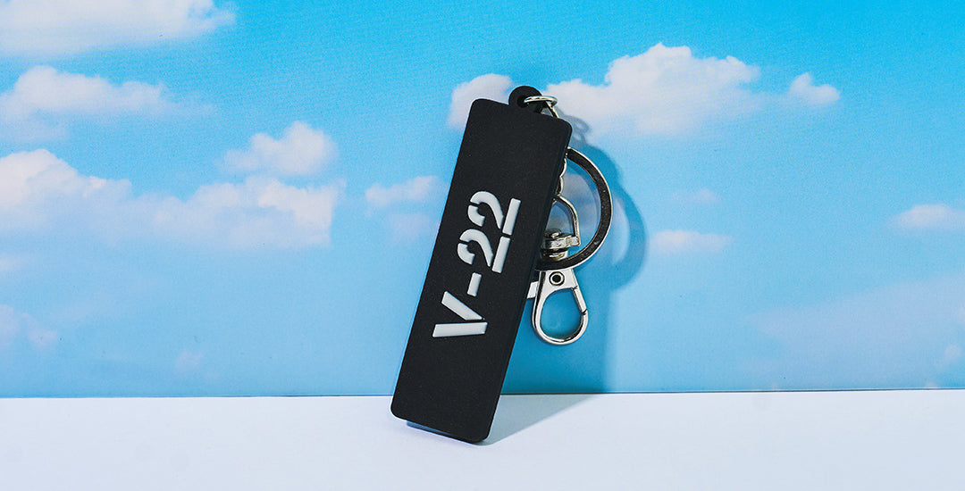 Boeing Series keychain with the V22 logo on the front, against a blue sky with clouds.