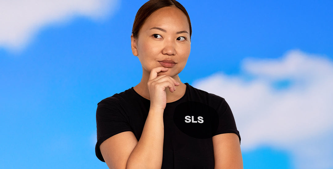 A person wearing a black Boeing Series T-shirt with the SLS logo on the left chest, standing against a blue sky with clouds.