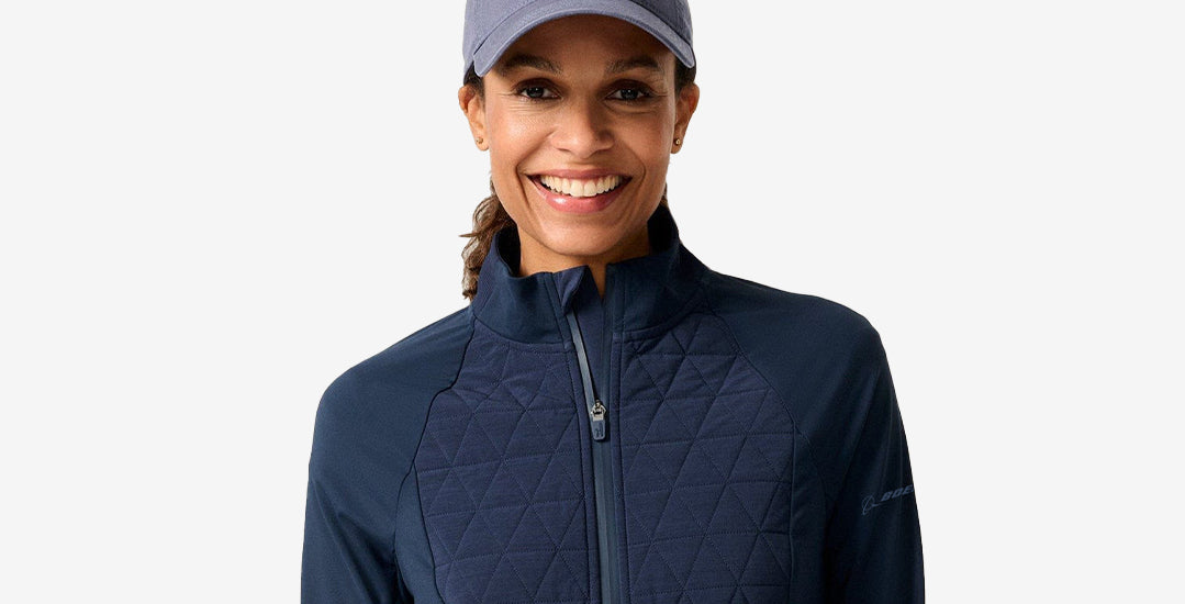 Woman wearing a navy quilted Boeing jacket and gray cap on a light gray background
