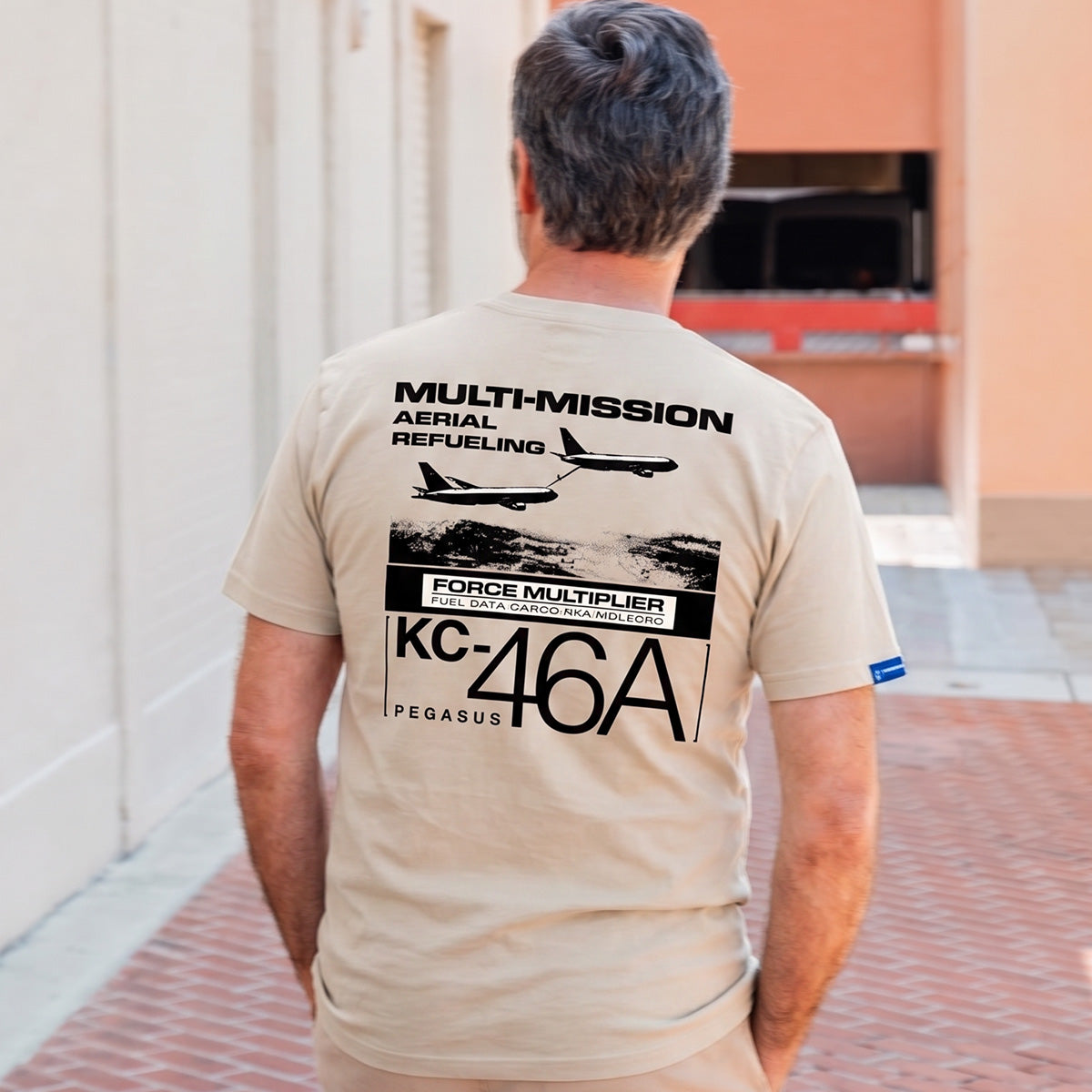 A man stands outside with his back to the camera, wearing the Boeing KC-46A Pegasus Unisex Graphic T-Shirt by BOEING—an ideal pick for aviation fans and Boeing enthusiasts.