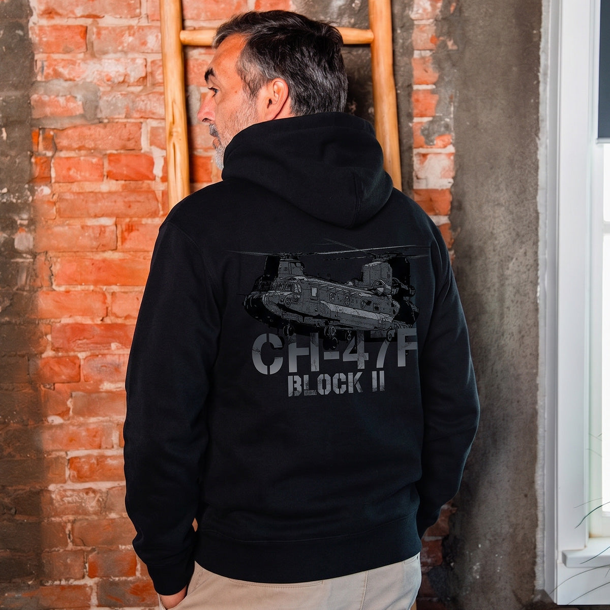 A man wears the Boeing CH-47F Block II Unisex Graphic Hoodie by BOEING, featuring a striking helicopter graphic and text, perfect for aviation enthusiasts and fans of Boeing apparel.