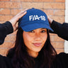 Aviation fans will love this image: a person in a black hoodie adjusts their BOEING F/A-18 Super Hornet Graphic Hat and smiles gently, with a brick wall behind them.