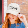 A smiling person with long red hair wears a BOEING KC-46A Pegasus Graphic Hat, touching its brim as they stand before a brick wall—an ideal accessory for fans of Boeing.