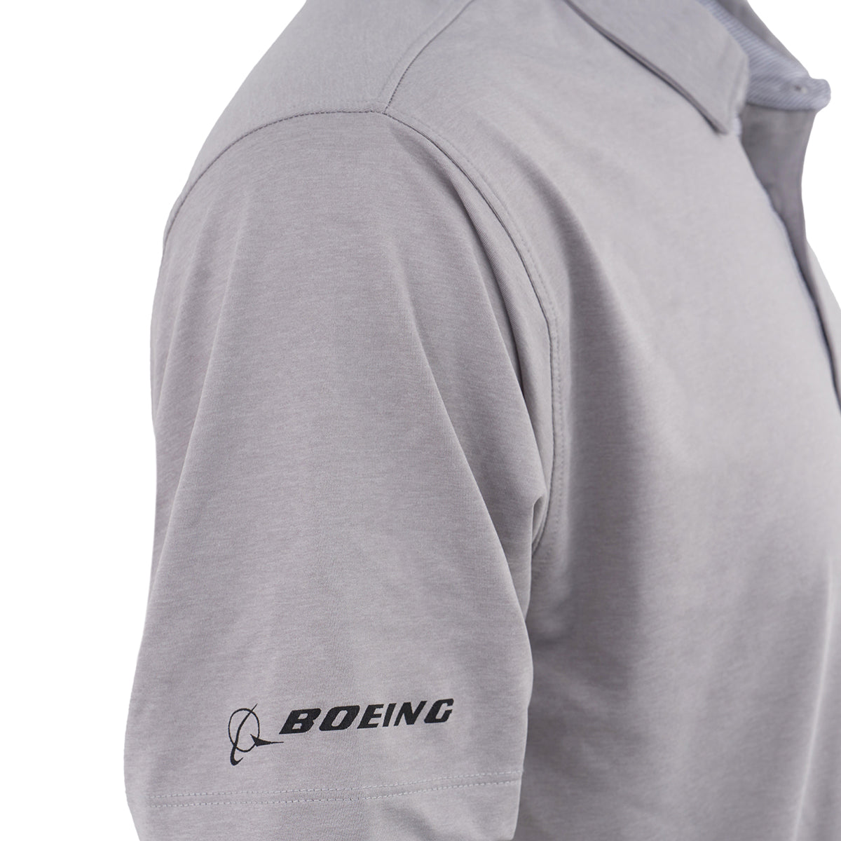 A close-up of a person wearing the Boeing P-8A Poseidon Series Men’s Polo by BOEING, a light gray moisture-wicking polo shirt with a collar, buttoned top, and the Boeing logo and text printed in black on the left sleeve.