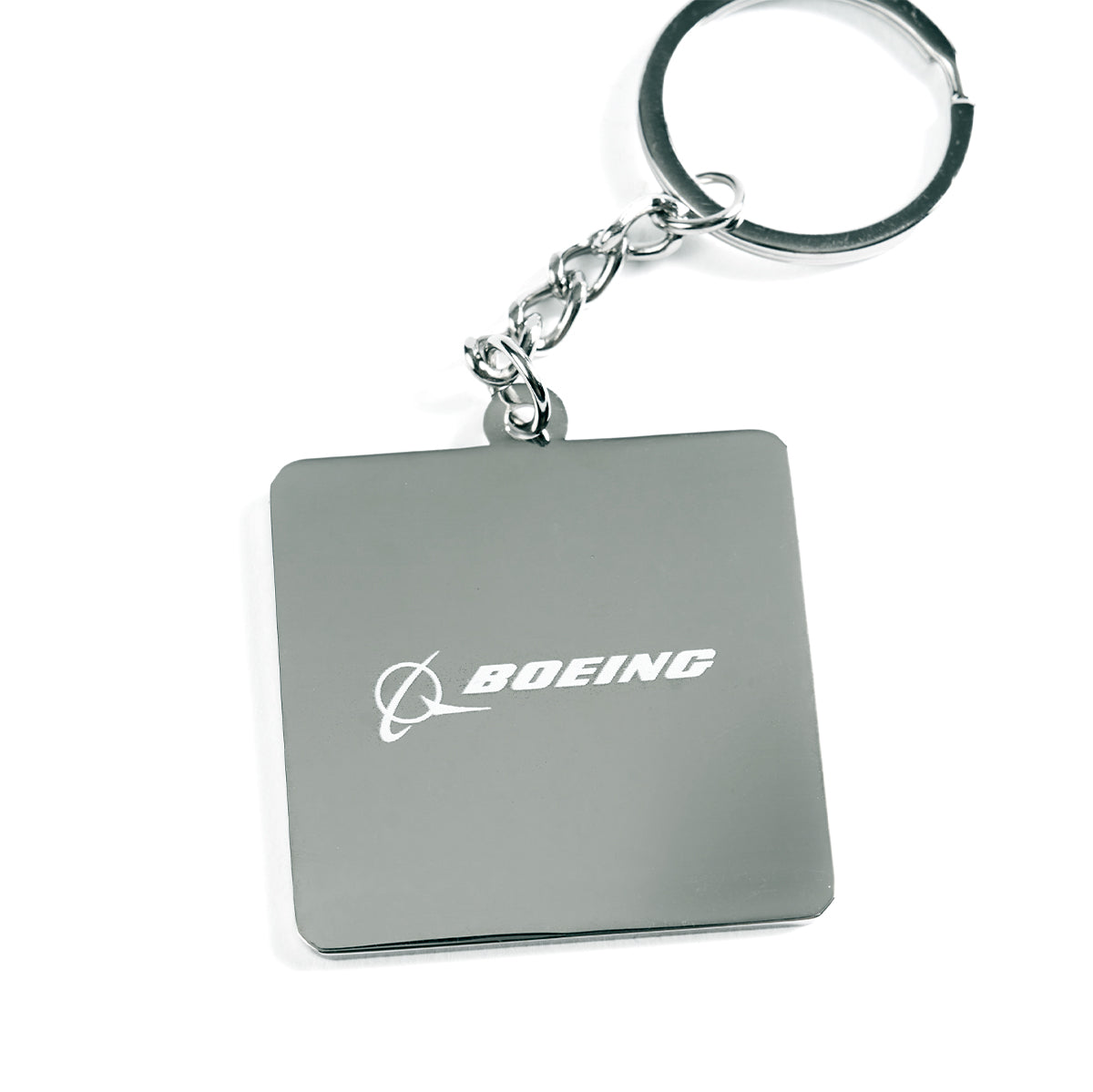 The Boeing 747 Motion Keychain by The Boeing Store features a square metallic tag with the Boeing logo and engraved text. This aviation-inspired piece, reminiscent of the iconic aircraft, hangs from a metal ring via a short chain on a white background.